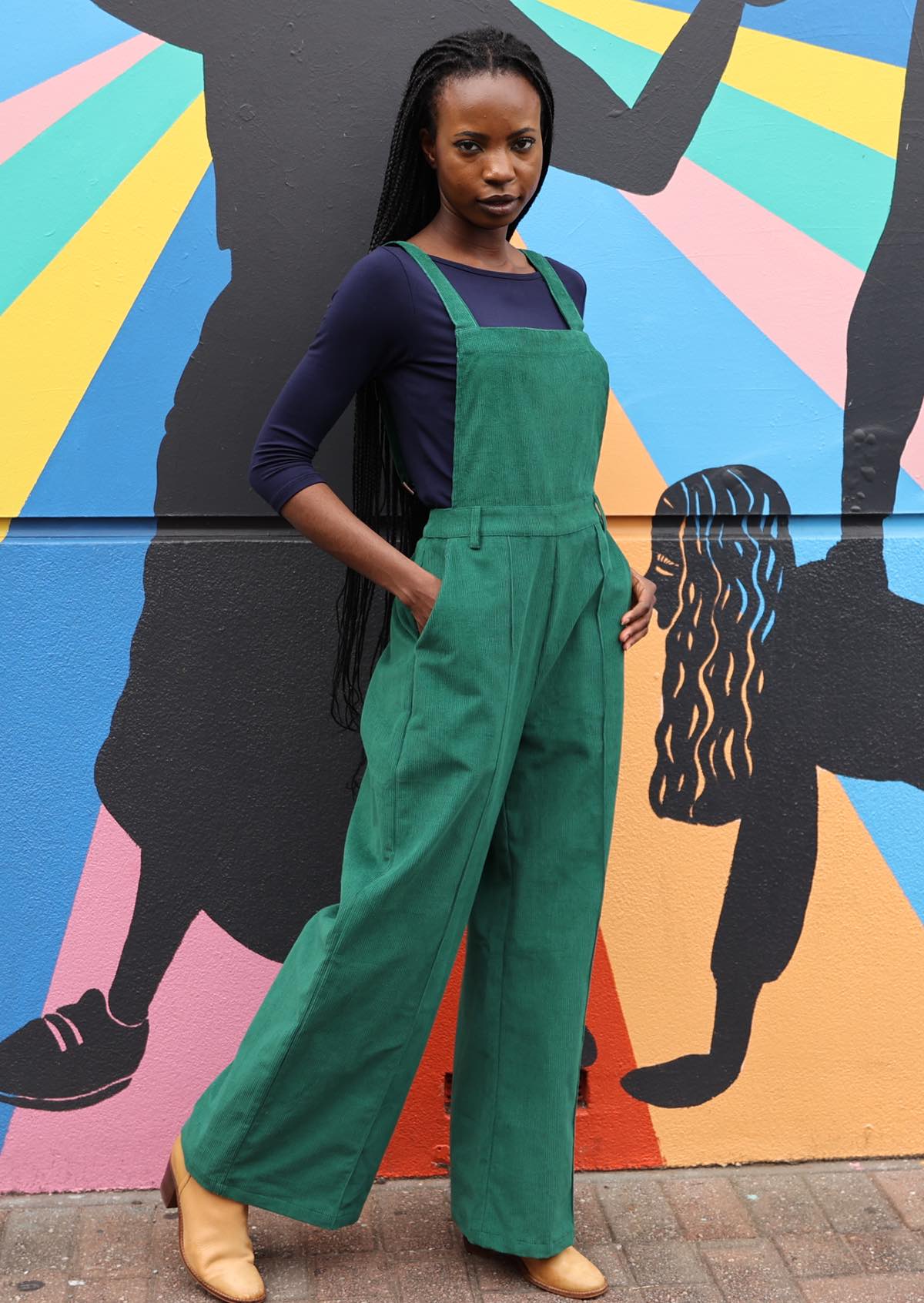 woman wearing hunter green cotton corduroy overalls with hands in pockets