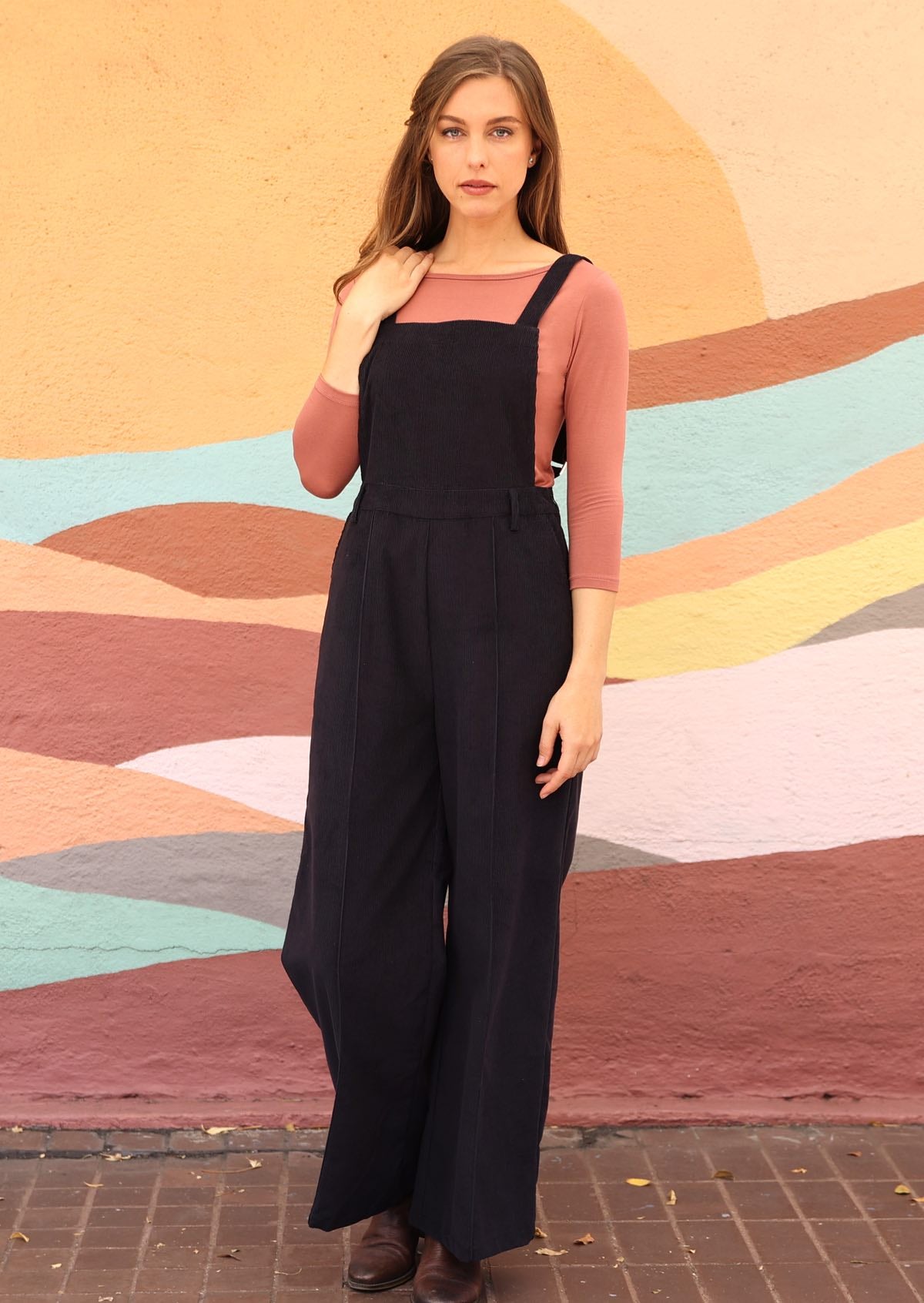woman wearing cotton corduroy overalls in dark grey over dusty pink long sleeve top