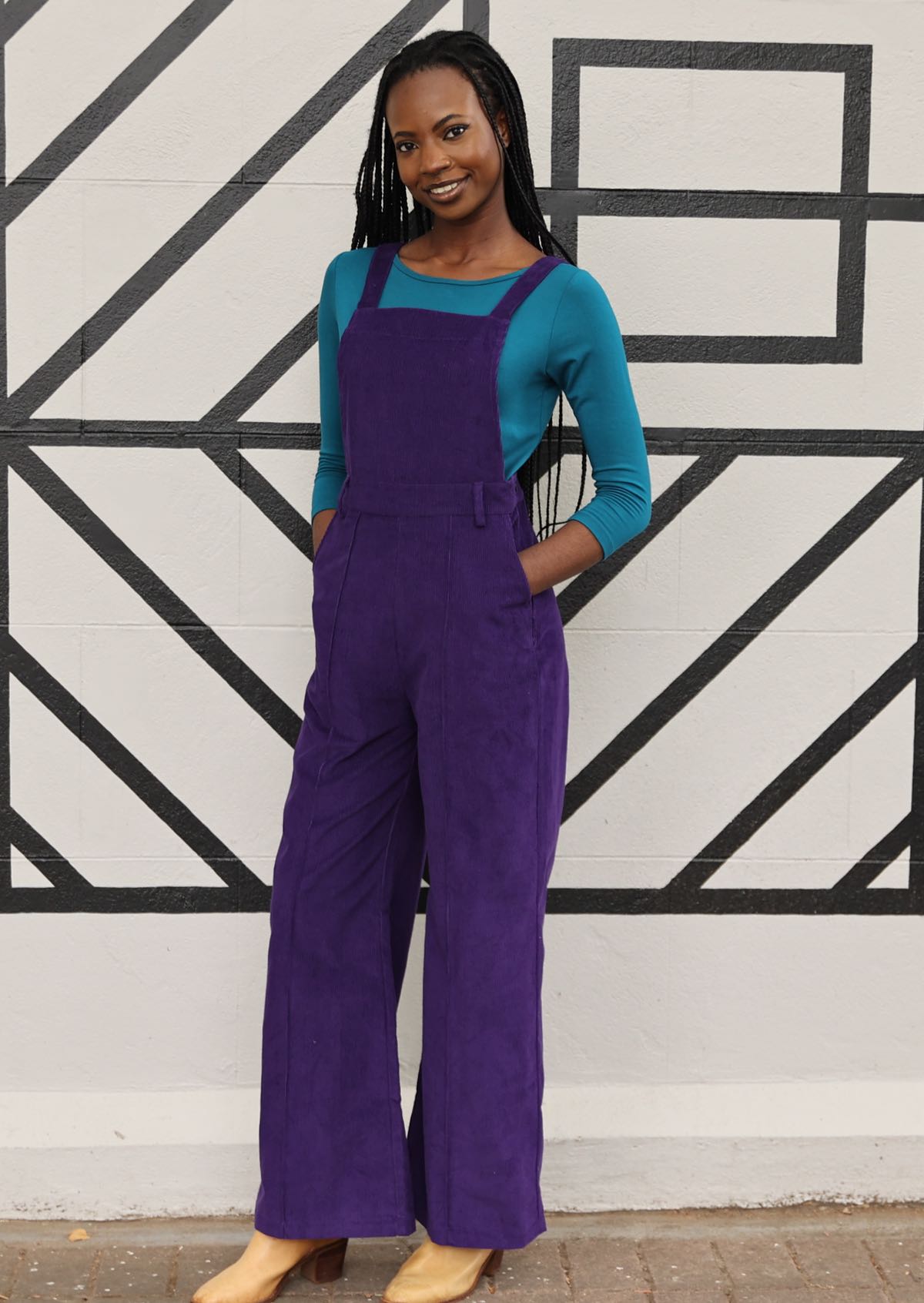 woman with teal top underneath purple cord overalls