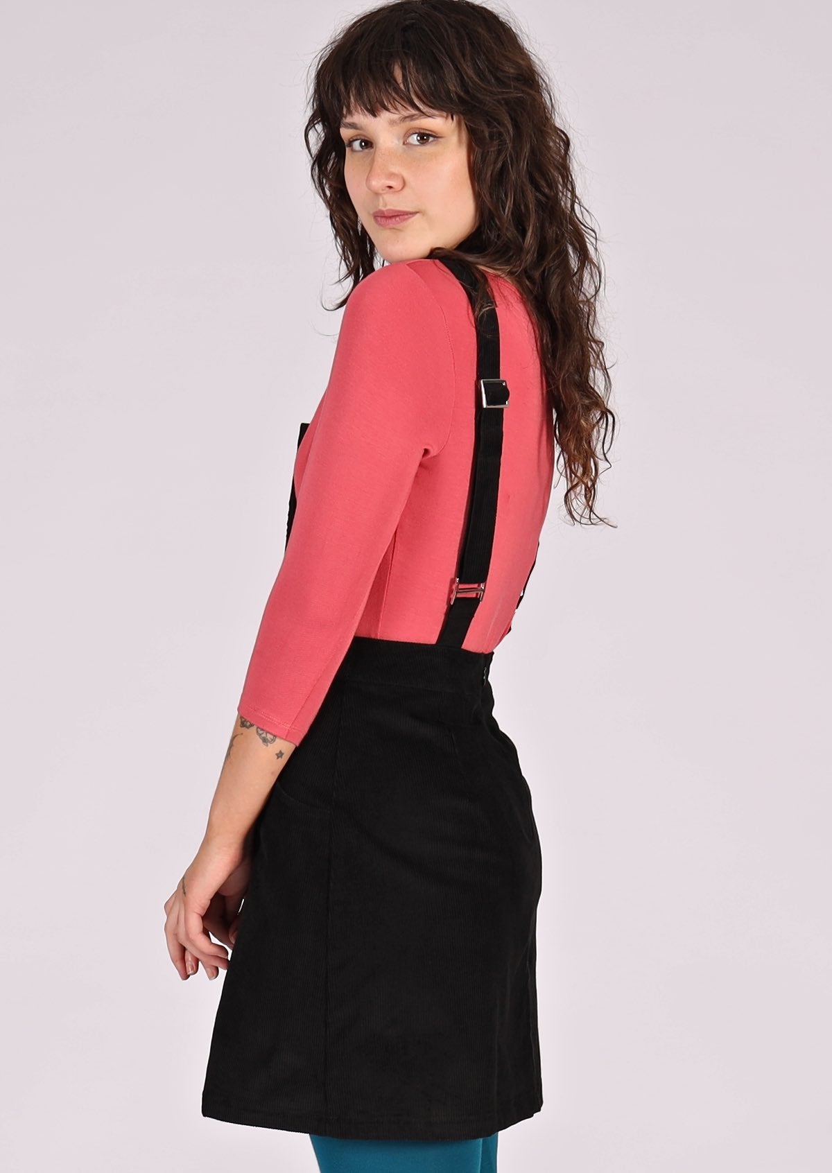 woman wearing black corduroy pinafore over pink top back view