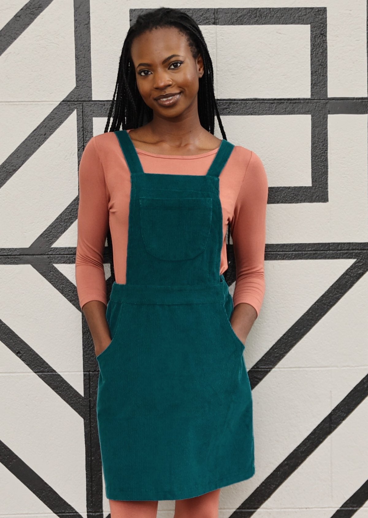 woman wearing teal corduroy pinafore over pale pink top