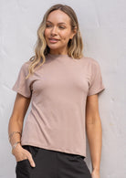 Woman wearing a beige t-shirt with a high crew neckline leaning against a wall