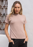 Woman wearing a beige t-shirt against a neutral background with hands in pockets of pants