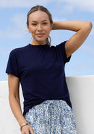 Woman wearing a navy blue t-shirt with a high crew neckline and floral skirt against a blue sky.