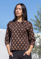 Woman wearing a brown Indian cotton patterned top with a clear blue sky and greenery in the background