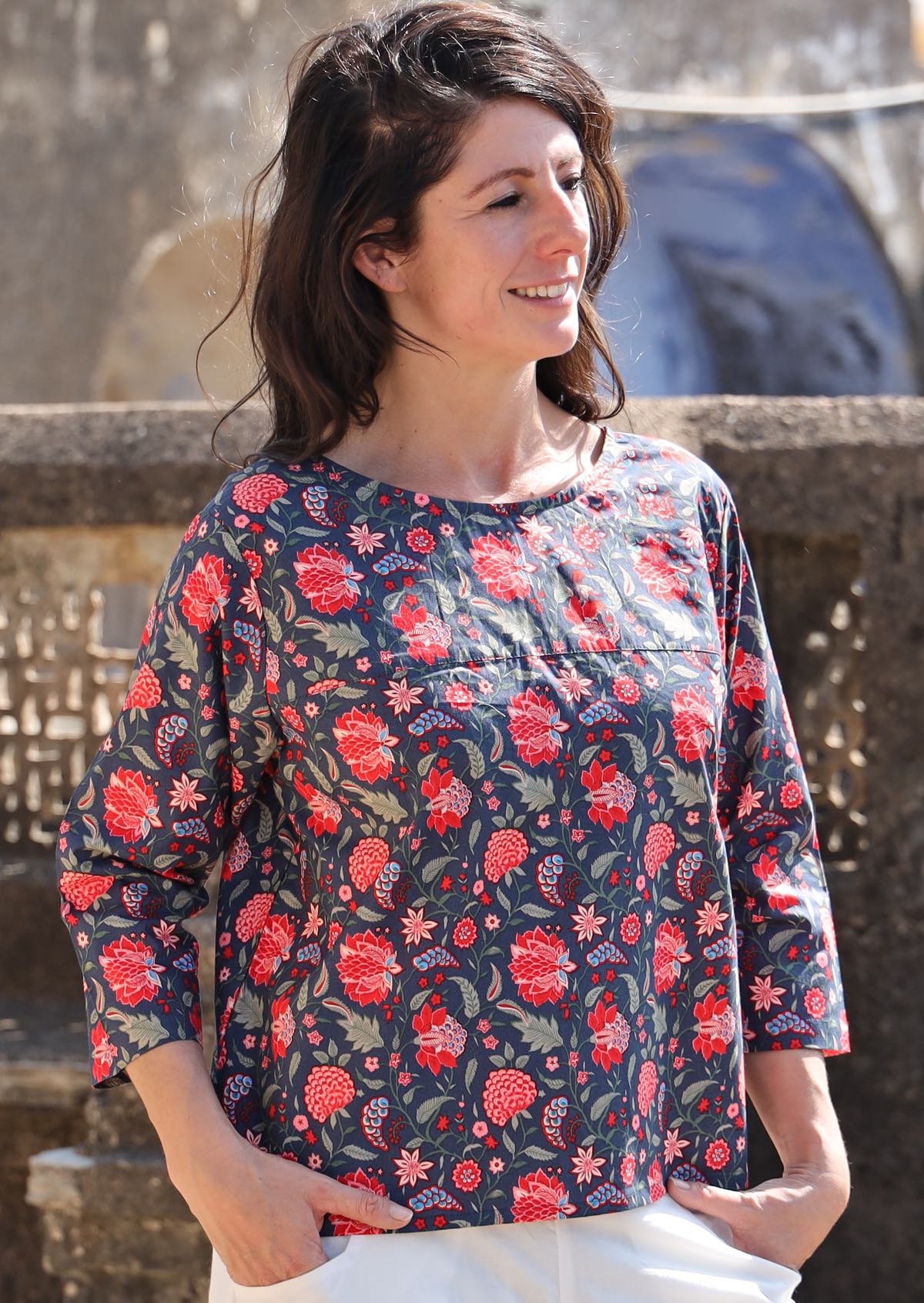 Model in a cotton relaxed fit 3/4 sleeve top in a red and green floral print on a blue base 