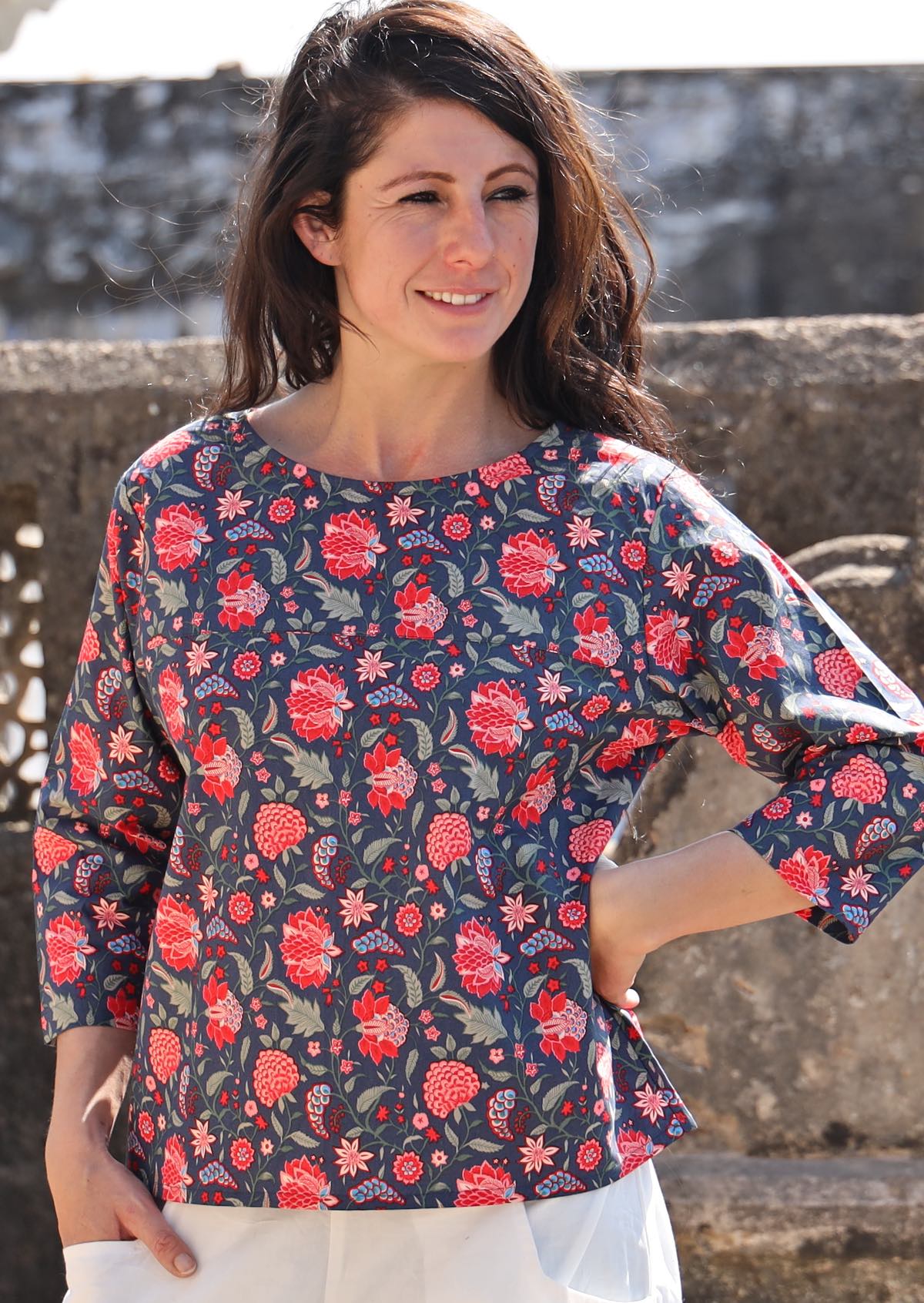 Woman in a cotton relaxed fit 3/4 sleeve top in a red and green floral print on a blue base 