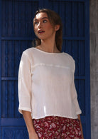 Woman wearing a white cotton top with floral pants against a blue wall.
