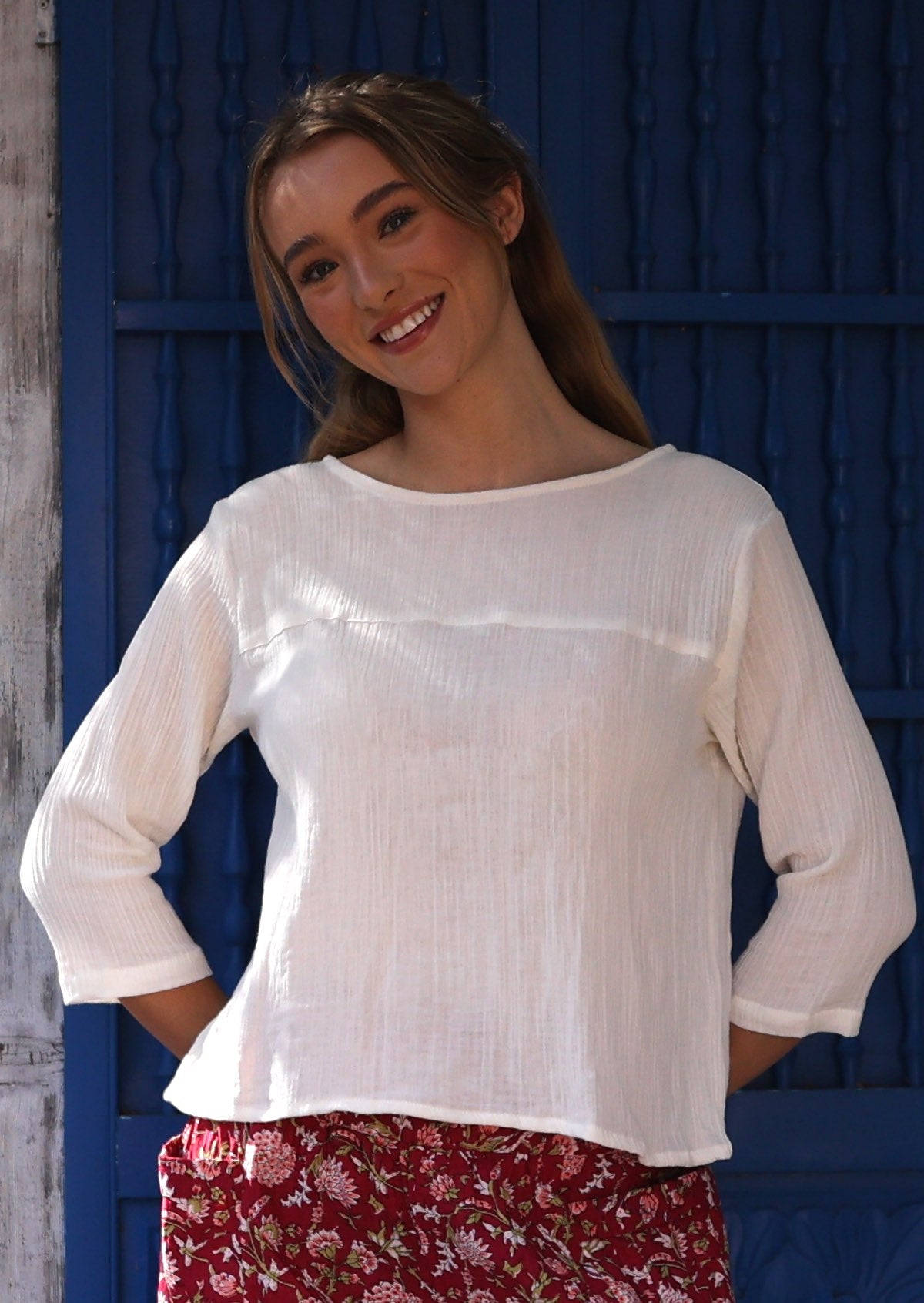 Woman wearing a white cotton top with 3/4 sleeves and a wide round neckline, paired with red floral pants