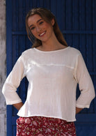 Woman wearing a white cotton top with 3/4 sleeves and a wide round neckline, paired with red floral pants