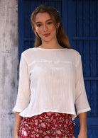 Woman wearing a white textured cotton top with a seam across the chest, a high round neckline and 3/4 sleeves