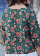 Back image of woman wearing relaxed fit cotton top with 3/4 sleeves and round neckline with decorative buttons on the back in green with a floral print