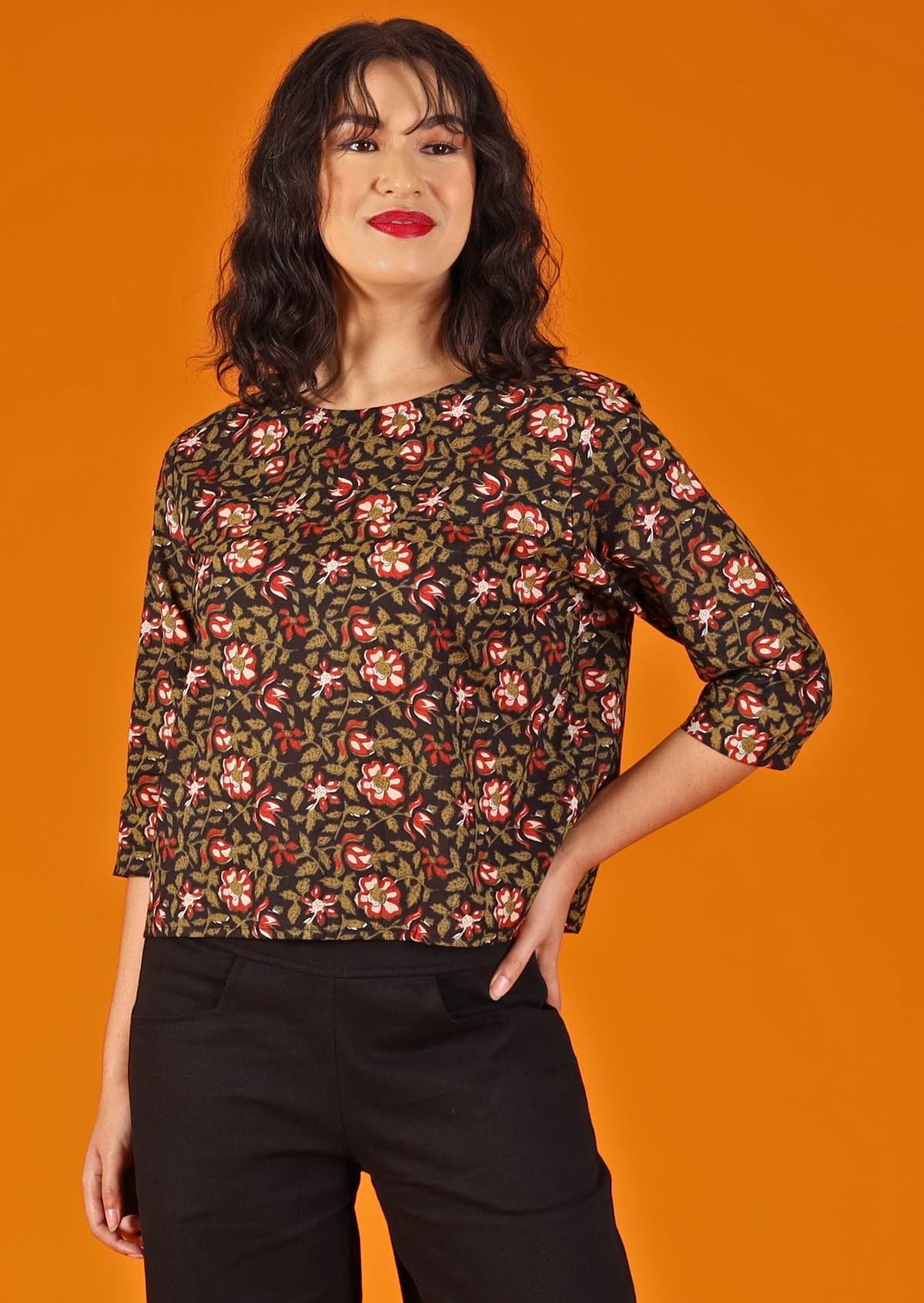 woman with dark hair and red lipstick in boxy cotton blouse, black base with  floral design 