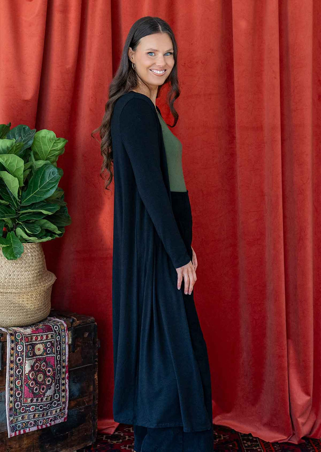 Woman wearing long black stretch jersey duster jacket over black corduroy pants and green v-neck top 