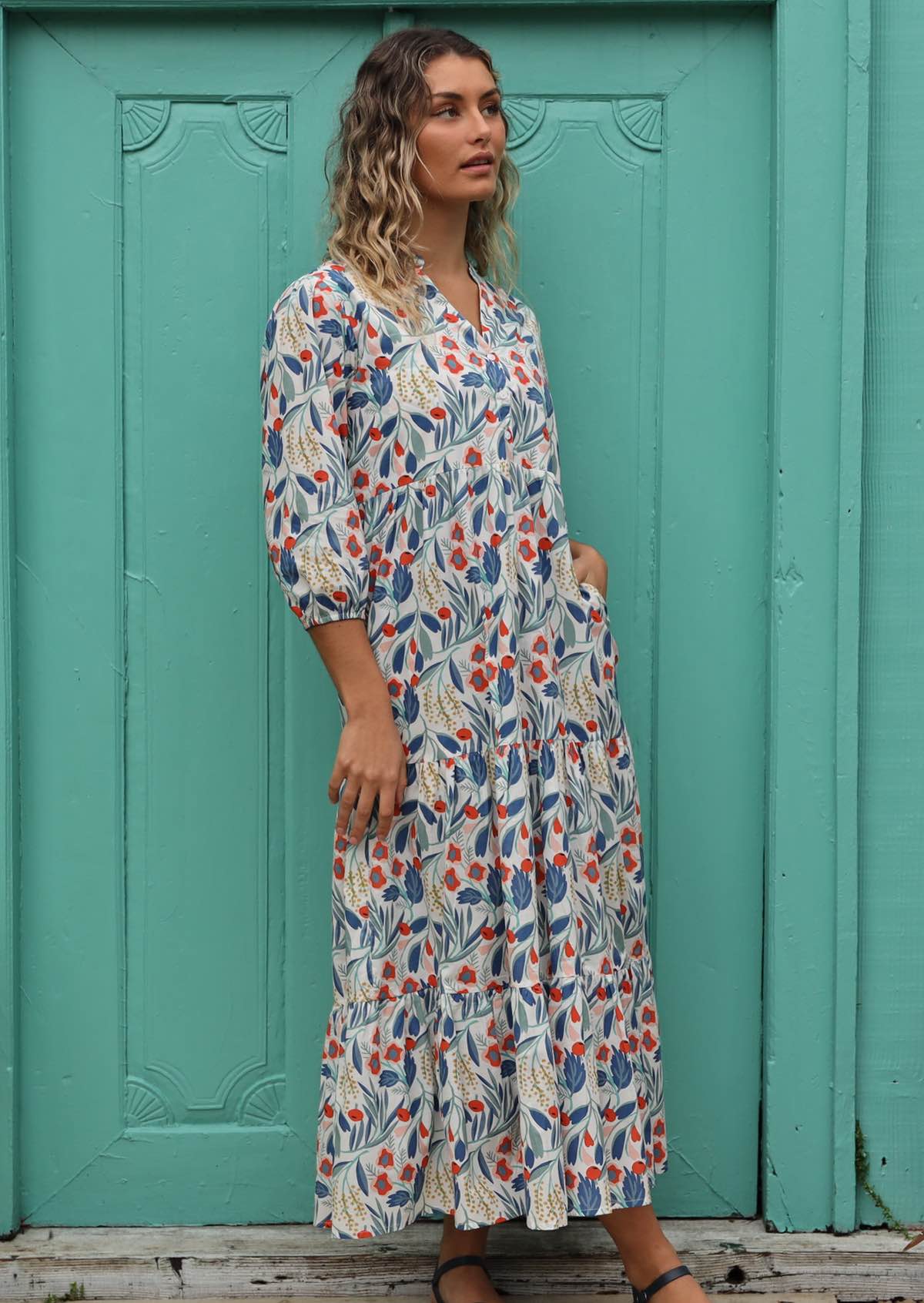 Model wears a flowing maxi dress with a floral print on a white base. 