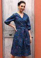 Model wears dress with green, orange and pink florals on a blue base. 
