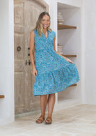 Woman holding skirt out to the side of a blue floral sleeveless, knee length dress with a V-neckline and buttoned bodice