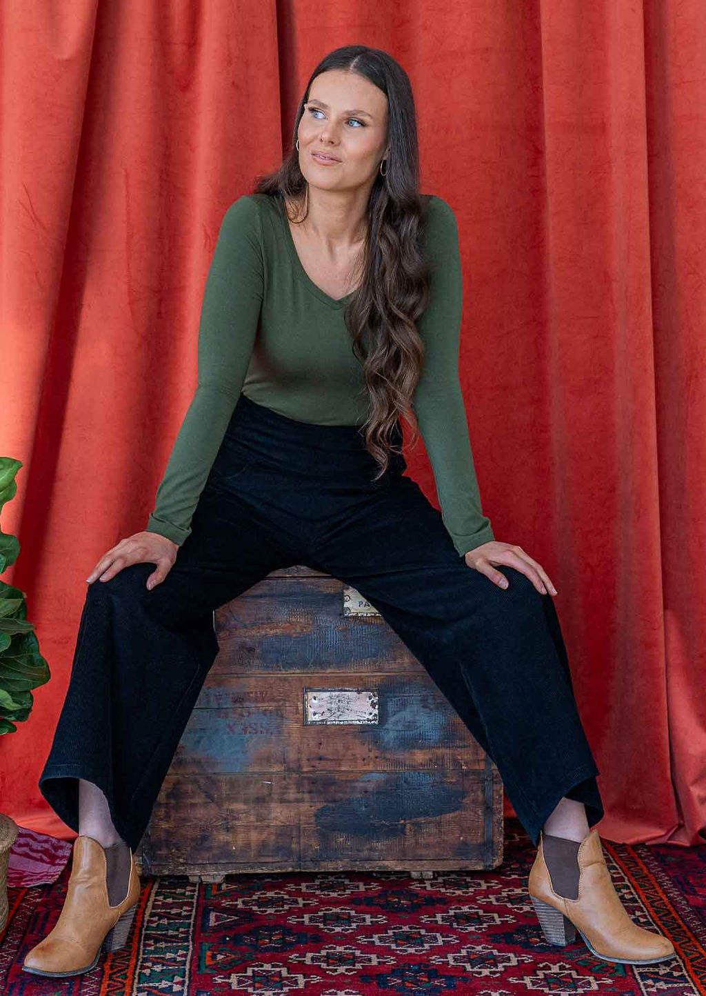 woman wearing black corduroy wide leg pants with hand on hip, paired with green long sleeve v-necked top