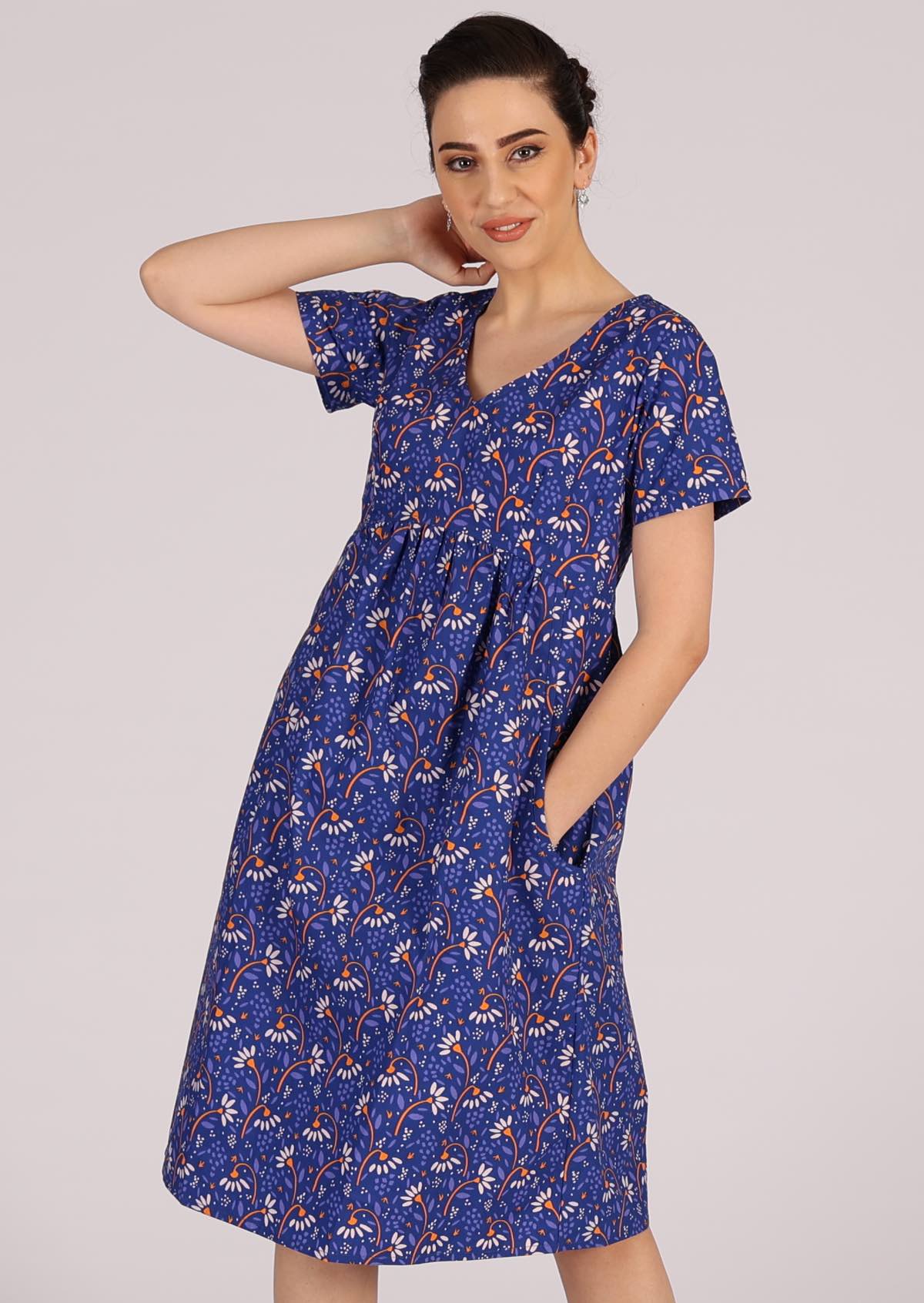 Smiling model wears blue based cotton dress with white and orange florals. 