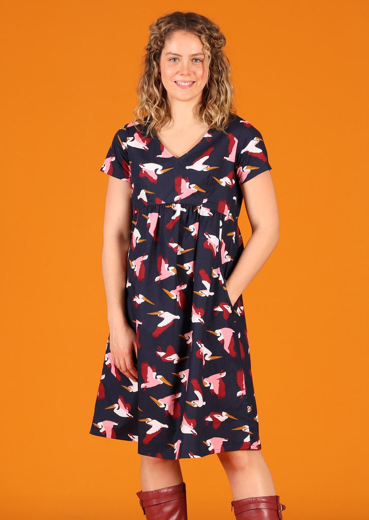 Model wearing Etta Dress Percival 100% cotton pelican print on dark blue base short sleeve v-neck knee length dress with side pockets 