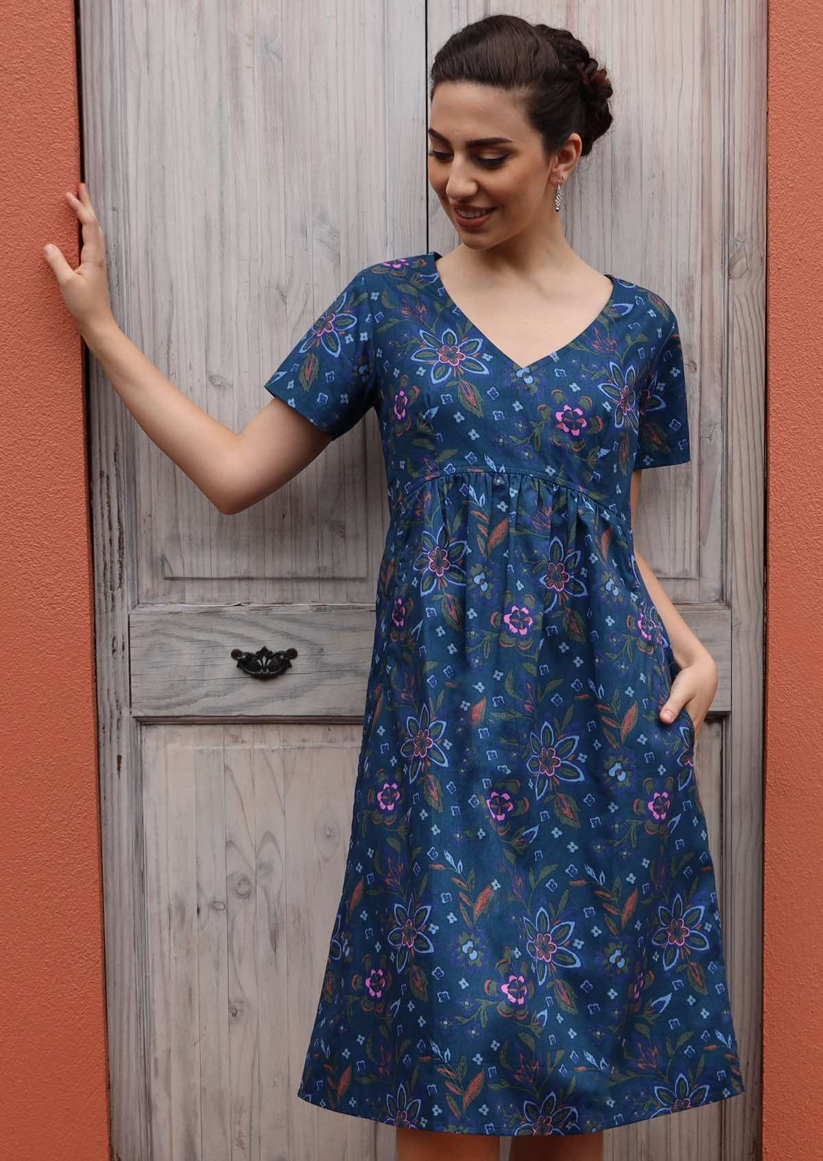 Model wears cotton floral blue dress that ends at the knee. 