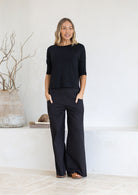 Woman wearing a black relaxed fit rayon top with black cotton pants standing in a minimalistic room