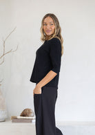 Woman wearing a black relaxed fit rayon top with 3/4 sleeves standing against a plain background