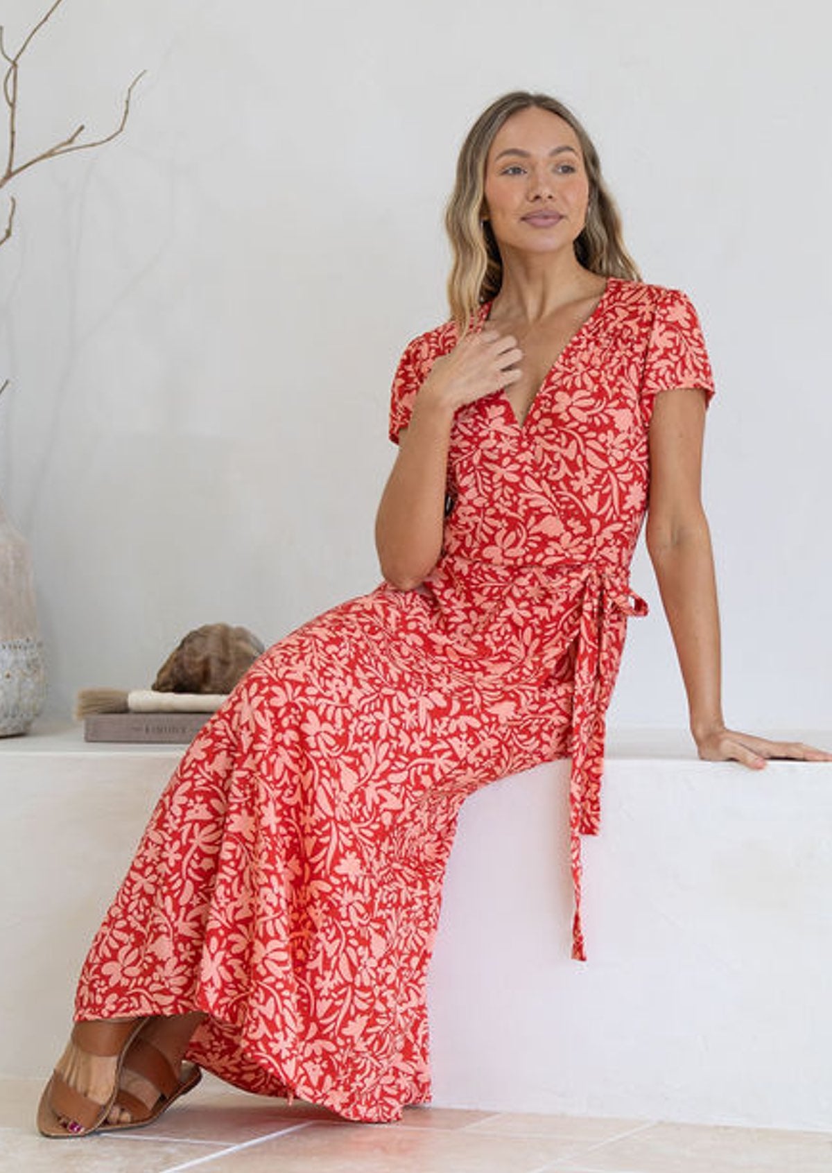 Woman wearing orange wrap around maxi dress seated on white bench 
