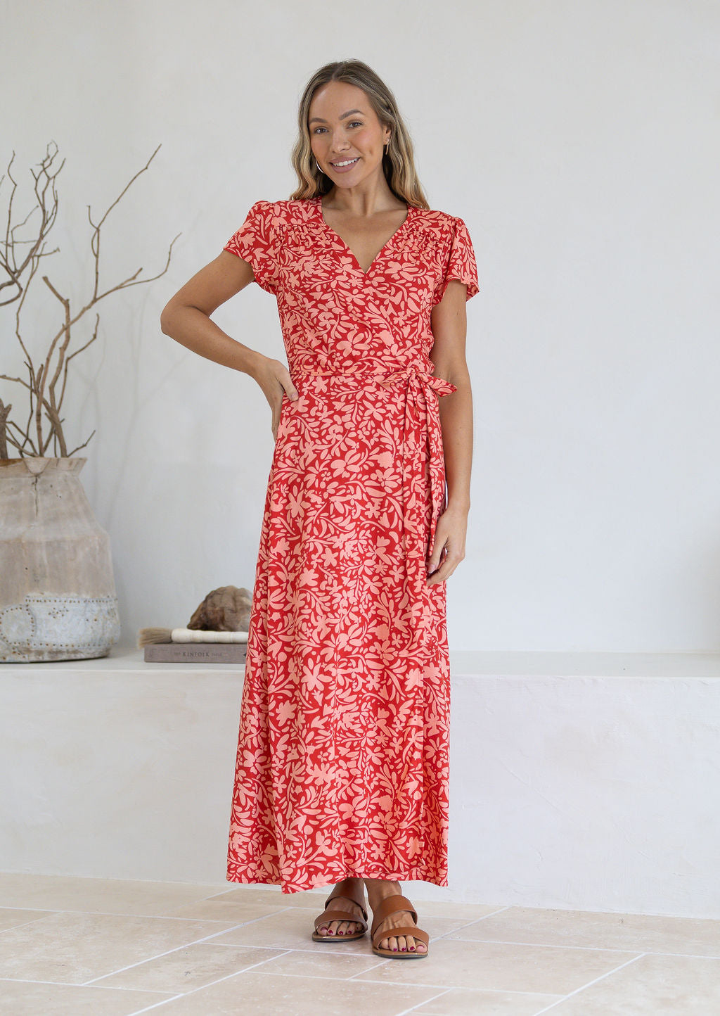 Woman wearing orange wrap around maxi dress with hand on hip 