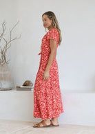 Woman wearing orange wrap around maxi dress with cap sleeves and tan sandals 