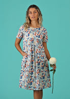 Model holds a flower and wears 100% cotton knee length dress. 
