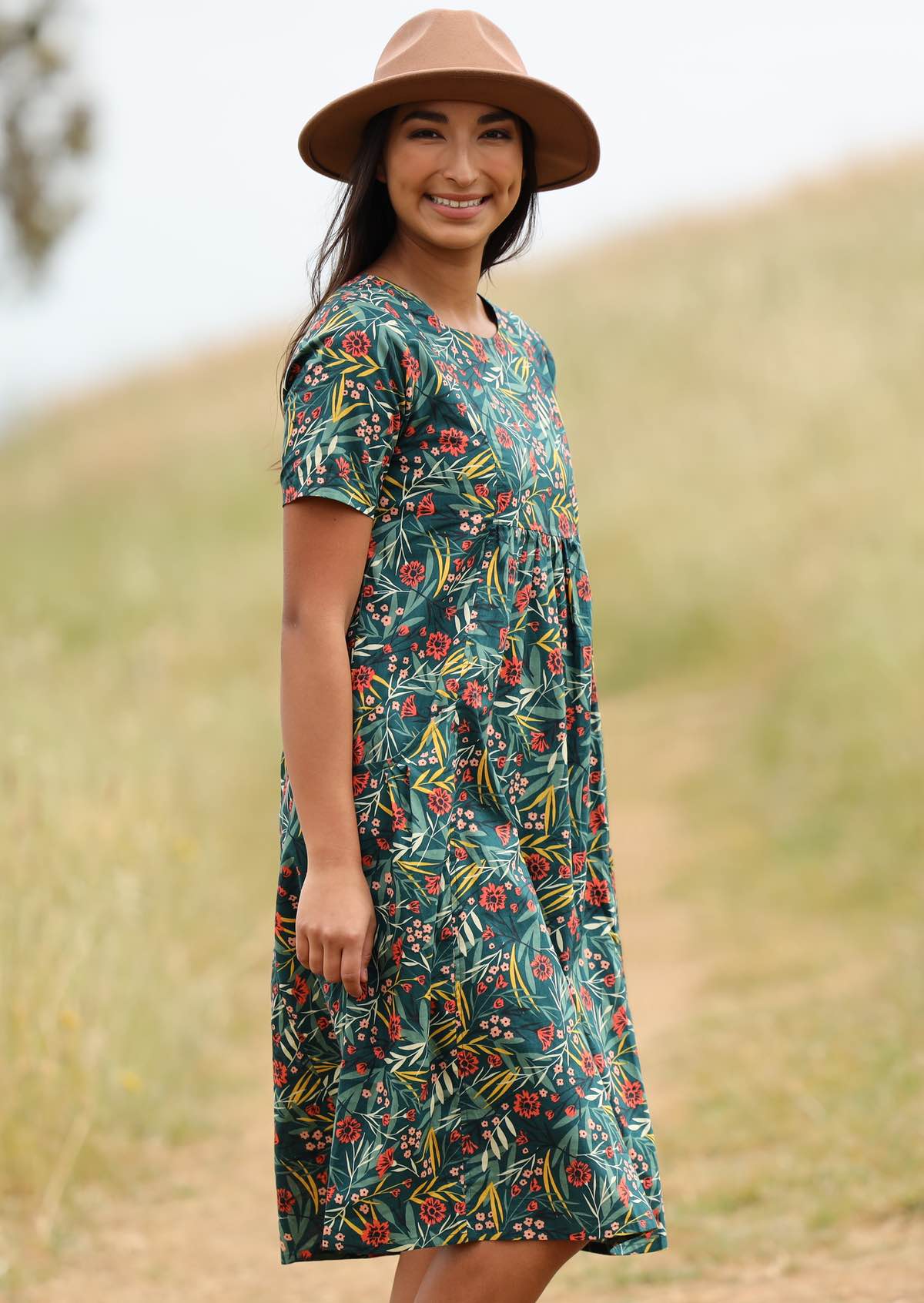 Smiling model pairs her floral dress with a hat for sun protection. 