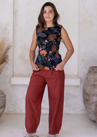 Woman standing with hands in pocket wearing a rust cotton pants with pleats at the ankles