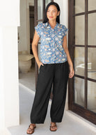 Woman wearing a blue floral top and black wide leg pants with hand in pocket