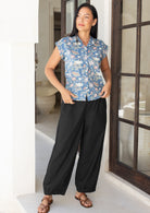 Woman wearing a blue floral shirt and black wide leg pants that taper at the ankle slightly