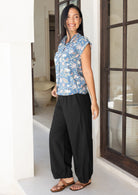 Woman wearing a blue floral shirt and black wide leg pants standing in a doorway.