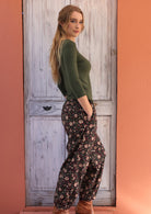 Woman standing sideways with hand in pocket wearing black based floral Indian 100% cotton pants