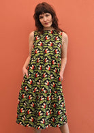 Model wears green, orange and white botanical print on black base cotton sleeveless 3 tiered dress with hidden side pockets 