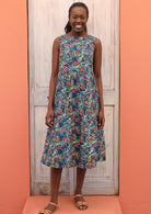 Model wears 100% cotton dress with a colourful floral pattern on a blue base. 