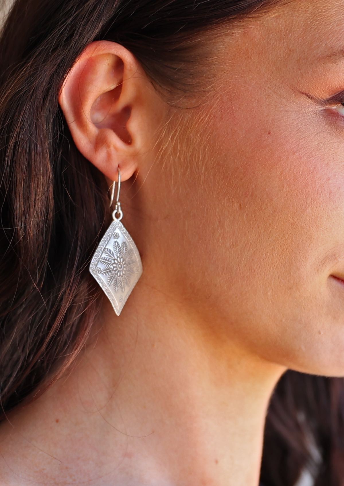 Close-up of a person wearing a Large Hill Tribe silver earring with a detailed design.