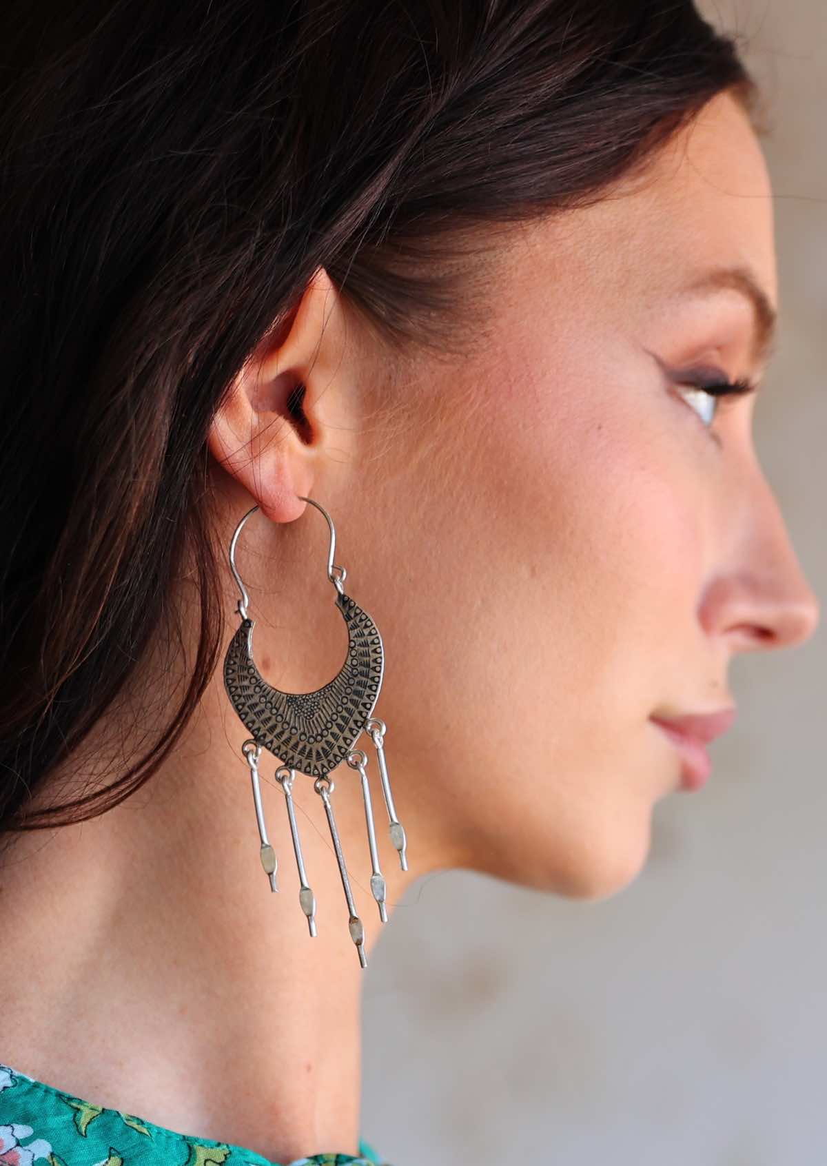 Close-up of a woman wearing large hooped Hill Tribe Silver earrings with dangling elements.