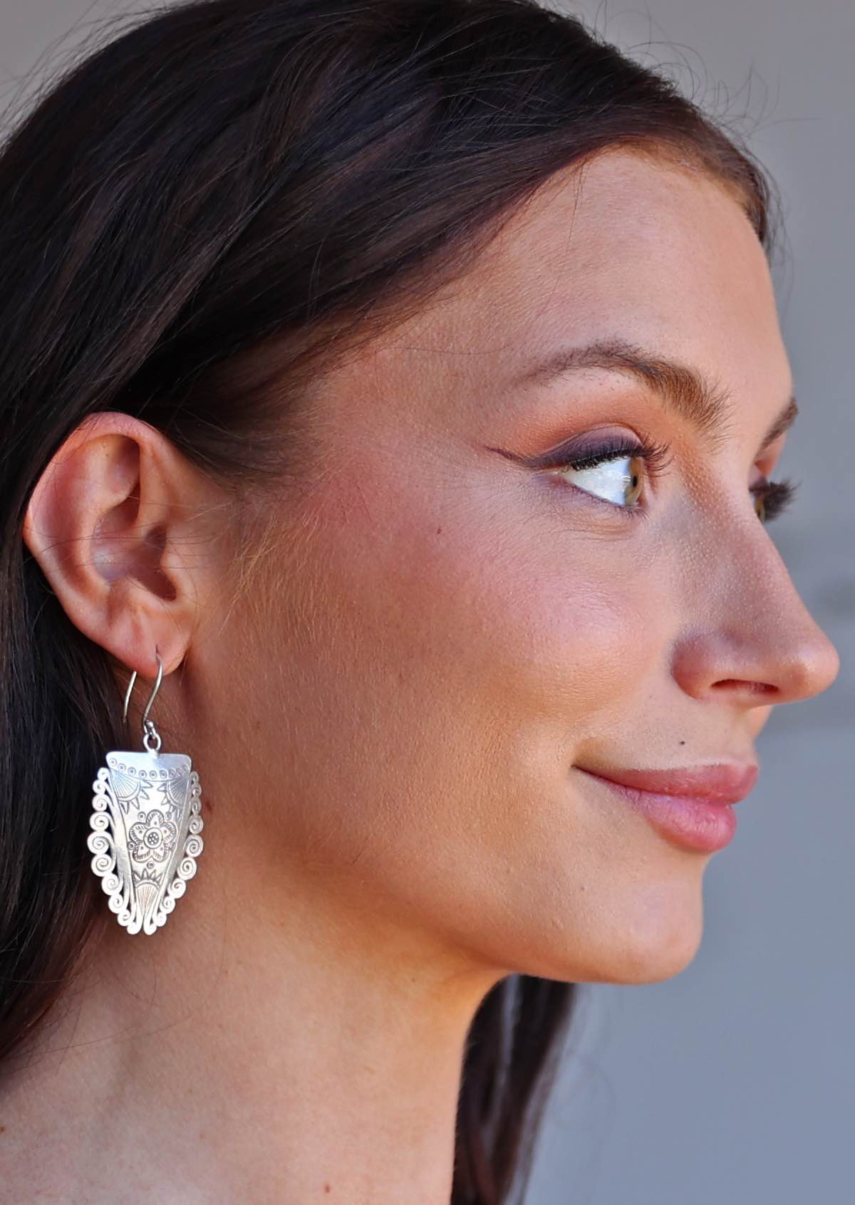 Close-up of a woman wearing Hill Tribe Silver Shield earrings with a neutral background
