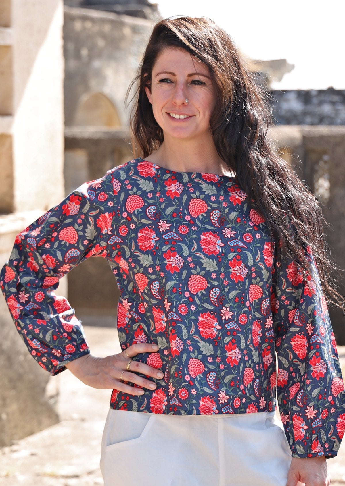 Woman wears cotton top with  bishop sleeves, in red and blue floral print with a boat neckline