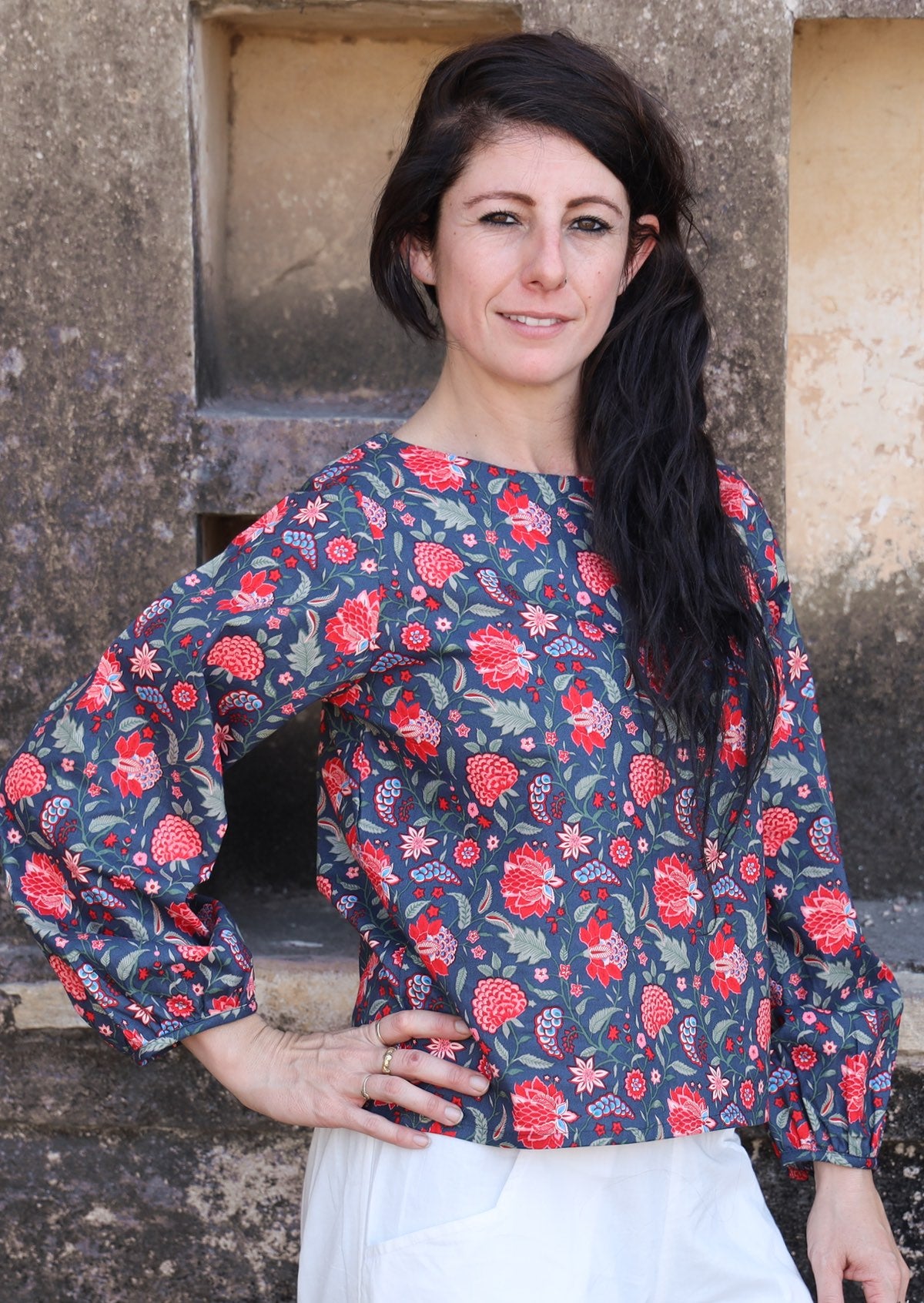 Model poses in cotton long sleeve top with bishop sleeves in red and green floral print on a navy base