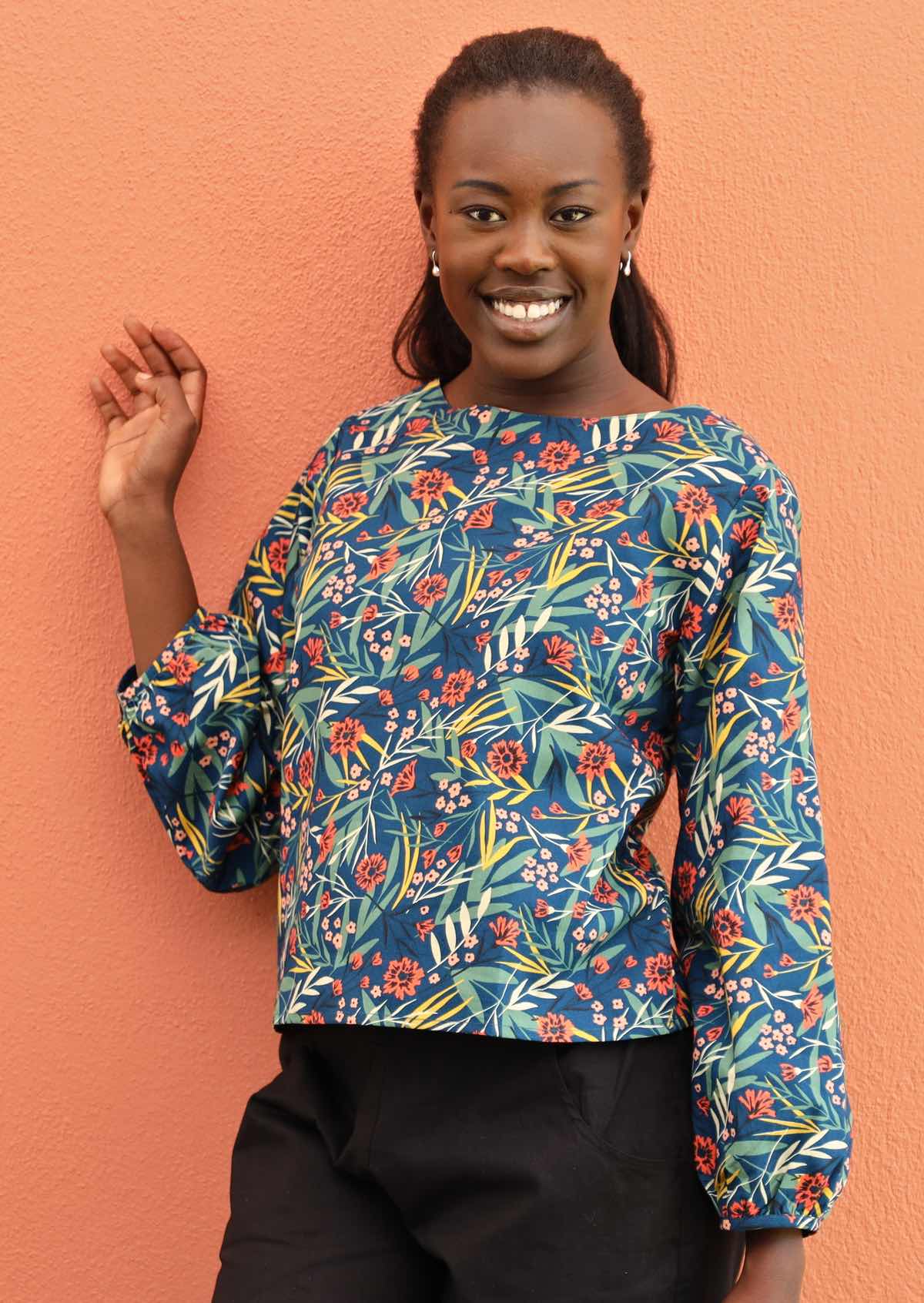 Happy woman wears a long sleeve top with a floral print on a blue base. 