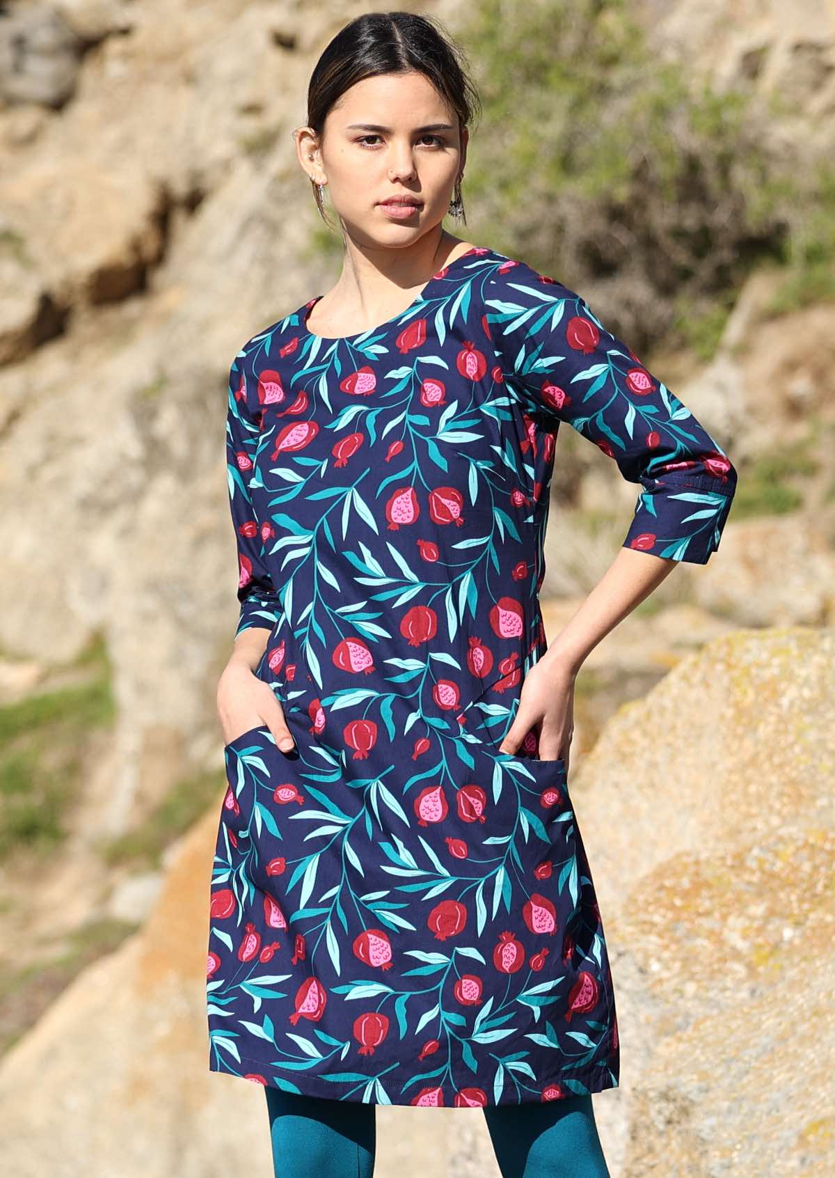Women wears 100% cotton 3/4 sleeve dress with a blue base fruit print. The dress has a round neck line and detail on the cuff.
