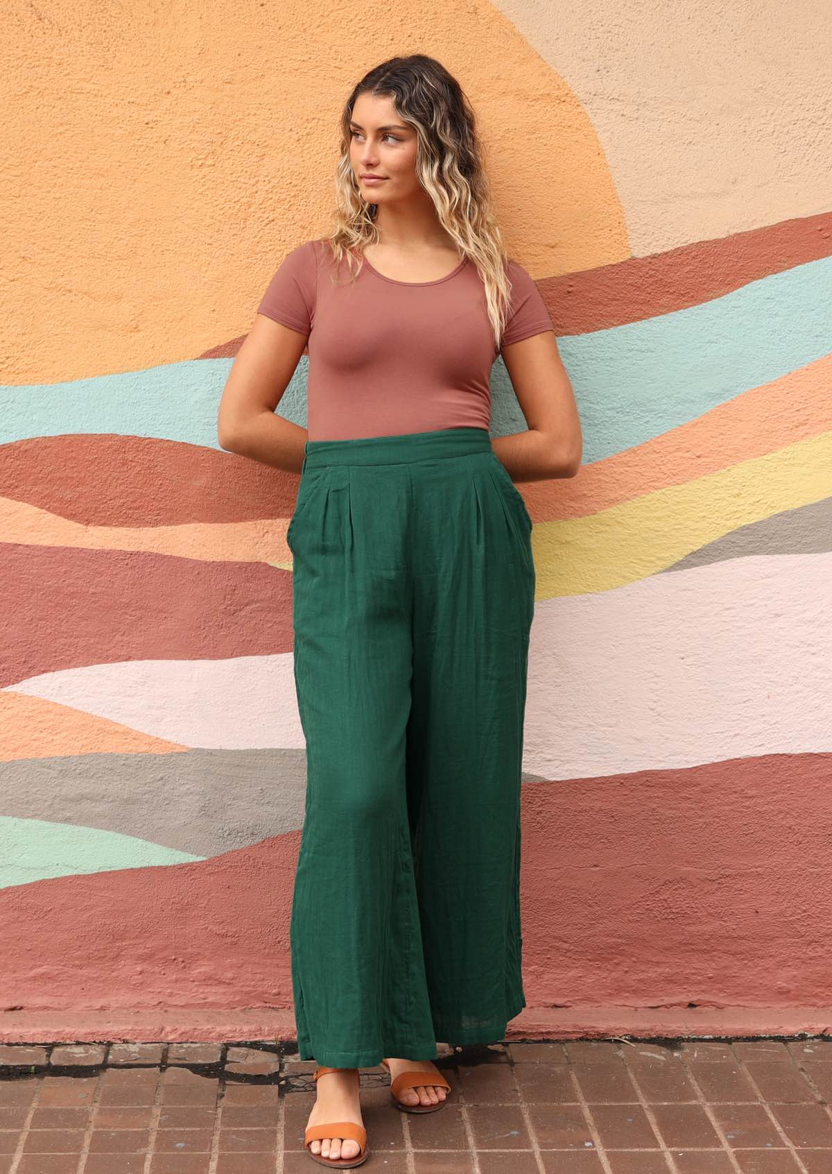 model leaning against wall wearing green pants, dusty pink shirt