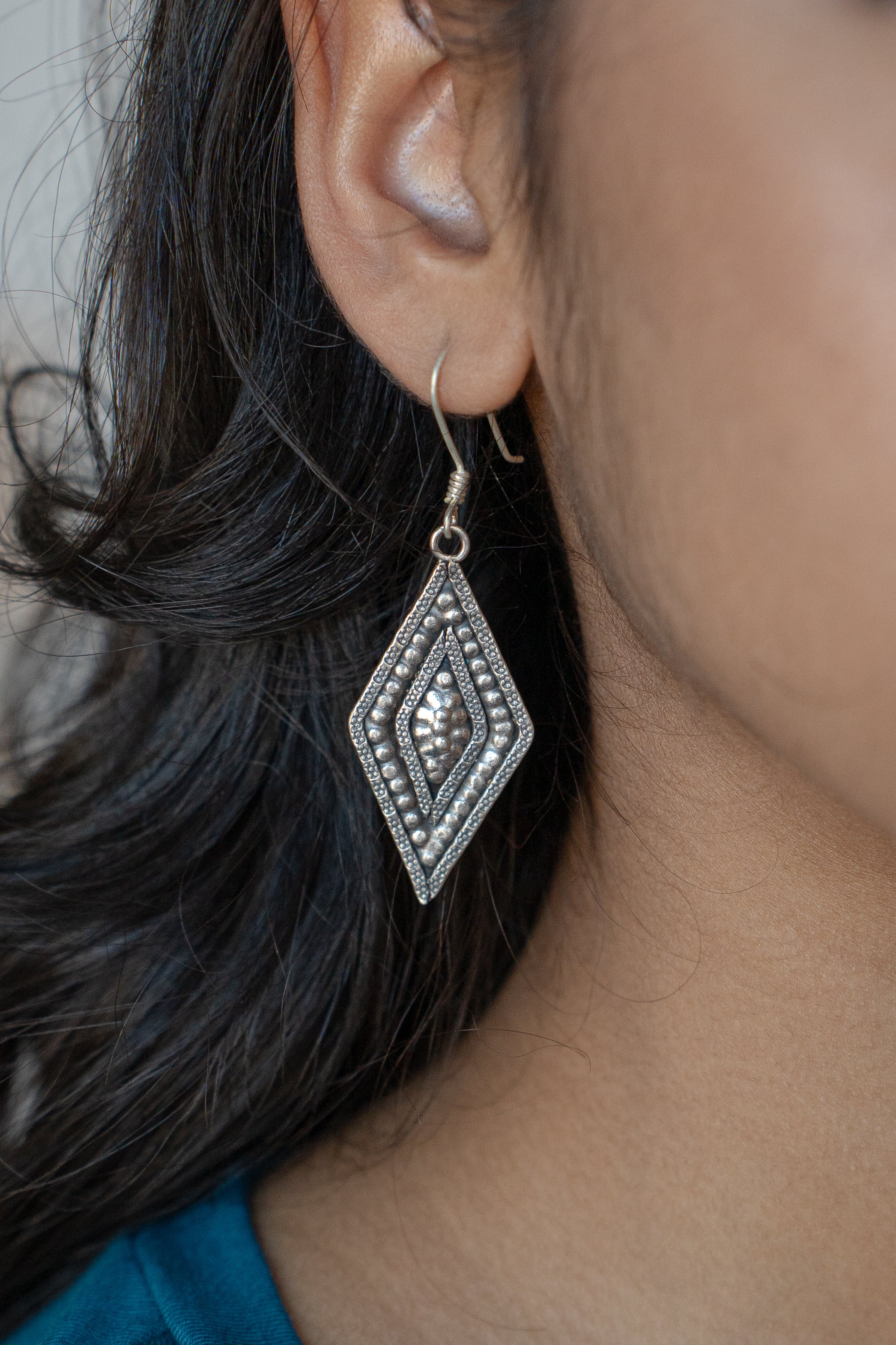 Close-up of a woman wearing Hill Tribe Silver diamond-shaped earrings with a blurred background