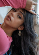 Woman with long dark hair wearing large silver hill tribe earrings, with a blurred background