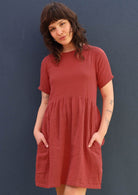 Model wears a loose fitting double cotton dress in a peachy terracotta colour. 